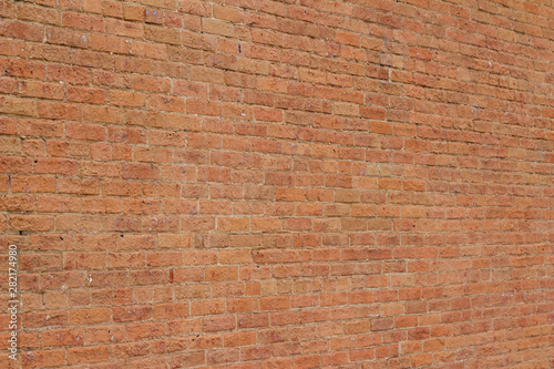 Old reddish orange brick wall background with cracks and worn texture (angle view)