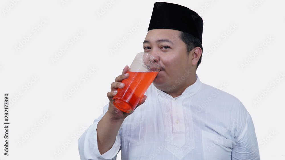 Fototapeta premium portrait of overweight muslim man with head cap or songkok drink a large glass of tea to break the fast
