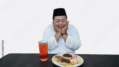 Portrait of overweight muslim man with head cap or songkok pray before eat and drink for islam break fasting