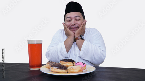Portrait of overweight muslim man with head cap or songkok pray before eat and drink for islam break fasting
