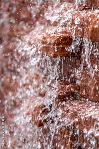 Close up view of glistening water running down a red brick stone wall
