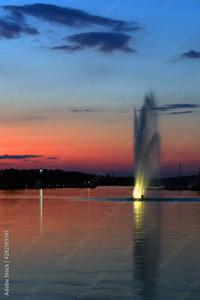 Sunset in Lappeenranta harbor in Finland. Lake with fountain and colorful summer evening sky. Vertical image.
