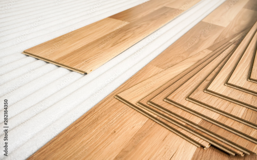 Tiles of light brown laminated floor with wooden effect laying on white base foam, ready to be installed Tiles of light brown laminated floor with wooden effect laying on white base foam, ready to be installed