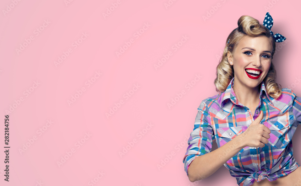 Pin up girl. Excited happy woman showing thumb up gesture or like sign.  Retro fashion and vintage concept. Pink color studio background. Stock  Photo