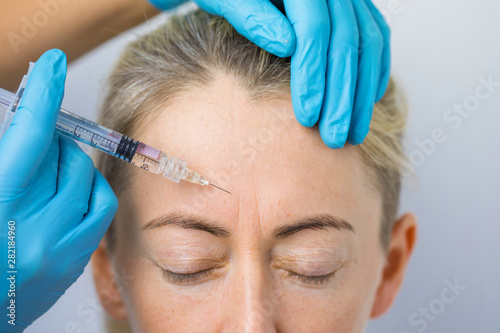 Doctor makes the rejuvenating facial injections for smoothing woman's forehead skin photo