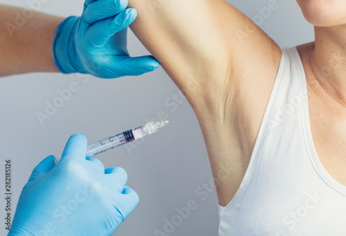 The doctor making intramuscular injection with syringe of botulinum toxin in the armpit against hyperhidrosis.