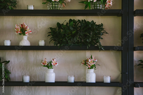 Black metal shelf with white vases with pink flowers and plants. © Juan.paz1