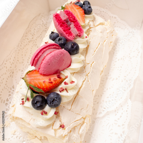 Meringue roll dessert decorated with berries and macaroons.