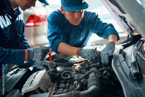 Fotografie Mechanic measuring level of motor oil when his coworker checking pipes