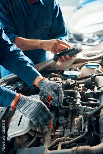 Hands of professional mechanics using professional tool for testing car motor in garage