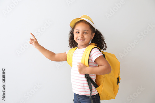 Portrait of stylish little African-American girl pointing at something on light background