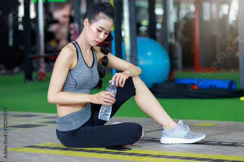 Fitness woman wearing headphone drinking water after cardio workout at fitness gym.