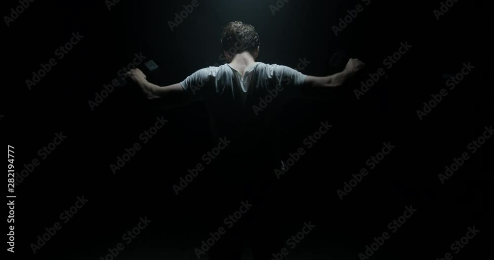 Active Male In A Dark Background Lifting Weights Away From Camera On Spotlight Preparing For Big Match Wearing White T-shirt Active Male In A Dark Background Lifting Weights Away From Camera On Spotlight Preparing For Big Match Wearing White T-shirt