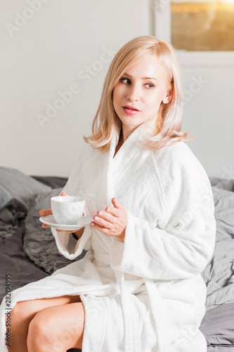 Woman in bathrobe relaxing in her bed in the morning with coffee