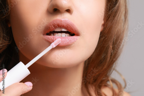Beautiful young woman applying lipstick against grey background, closeup