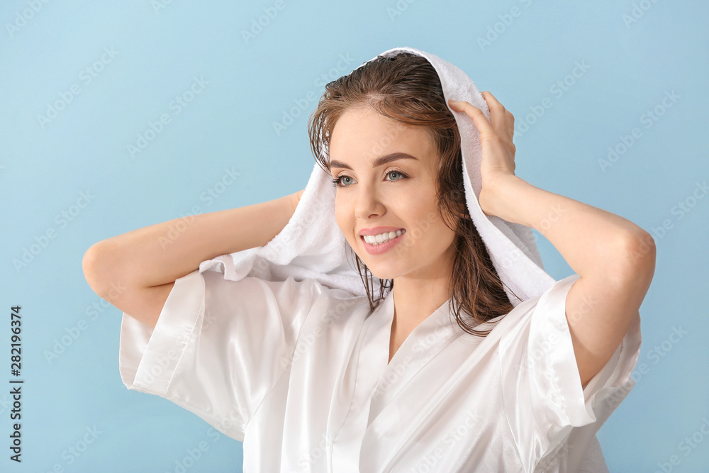 Beautiful young woman wiping hair after washing against color background