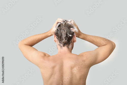 Handsome young man washing hair against grey background, back view