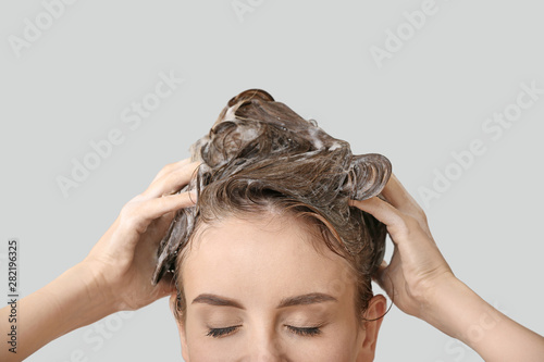 Beautiful young woman washing hair against grey background