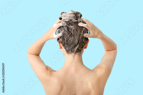 Beautiful young woman washing hair against color background, back view