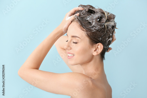Beautiful young woman washing hair against color background