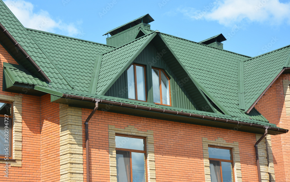 Metal house roof with attic window, roof gutters and brick walls