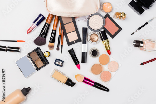 A pink makeup bag with cosmetic beauty products spilling out on to a light background, with empty space at side
