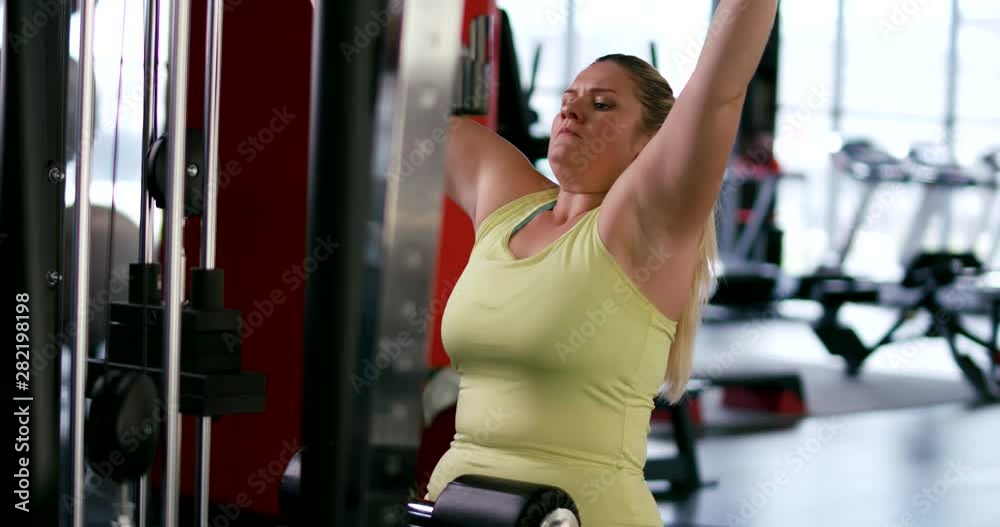Plus Size Model, woman trains in Gym, lifting blocks on rack machine, training muscles on block device and gym equipment. Plus Size Model, woman trains in Gym, lifting blocks on rack machine, training muscles on block device and gym equipment.