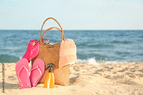 Bag with flip-flops, swimsuit, towel, sunglasses and cosmetics on sand beach