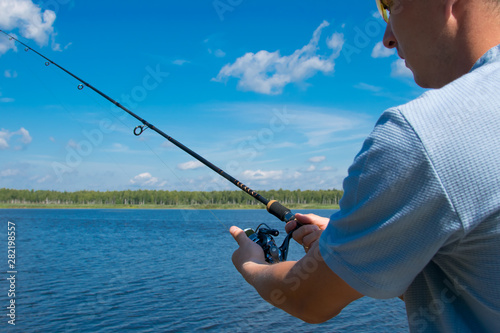 close-up, a man in yellow glasses holding spinning, for fishing, against a blue lake and sky