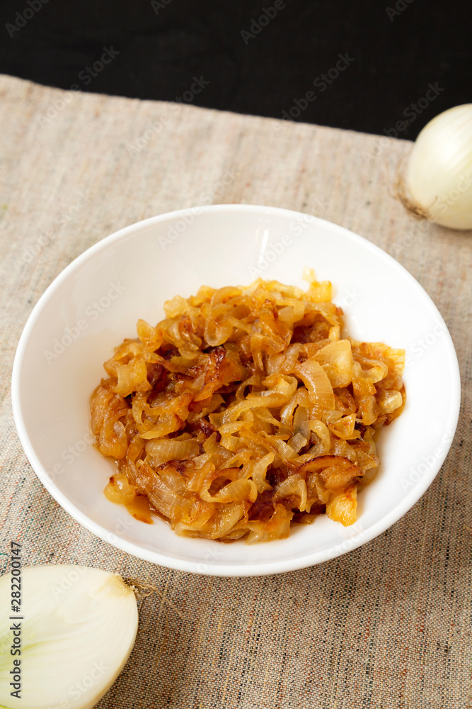 Homemade caramelized onions on a white plate on a black surface, side view. Close-up. Homemade caramelized onions on a white plate on a black surface, side view. Close-up.