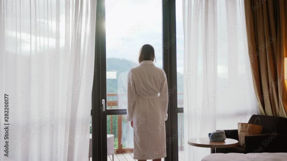 Close up back view young woman opening curtain lace standing in luxury apartment home or hotel looking through window enjoying wellbeing light city skyscrapers morning close up slow motion