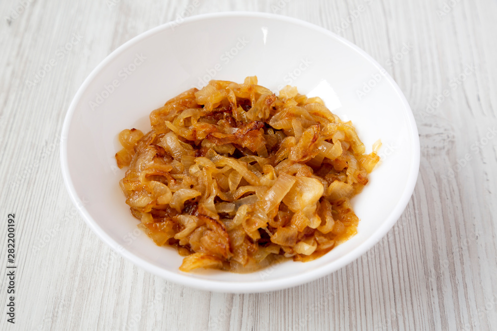 Homemade caramelized onions on a white plate on a white wooden surface, side view. Close-up.