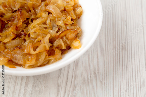 Homemade caramelized onions on a white plate on a white wooden surface, side view. Copy space.