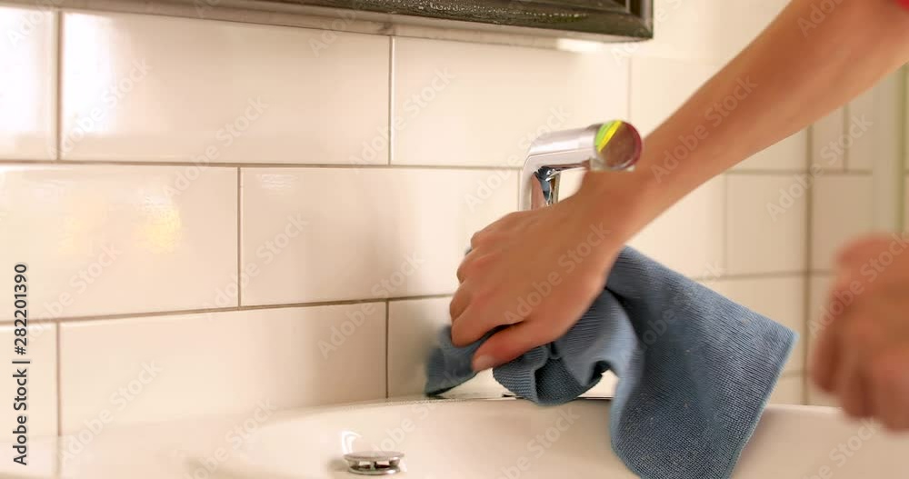Side view of hands cleaning steel shiny water tap with blue soft rag in white sink in bathroom Side view of hands cleaning steel shiny water tap with blue soft rag in white sink in bathroom
