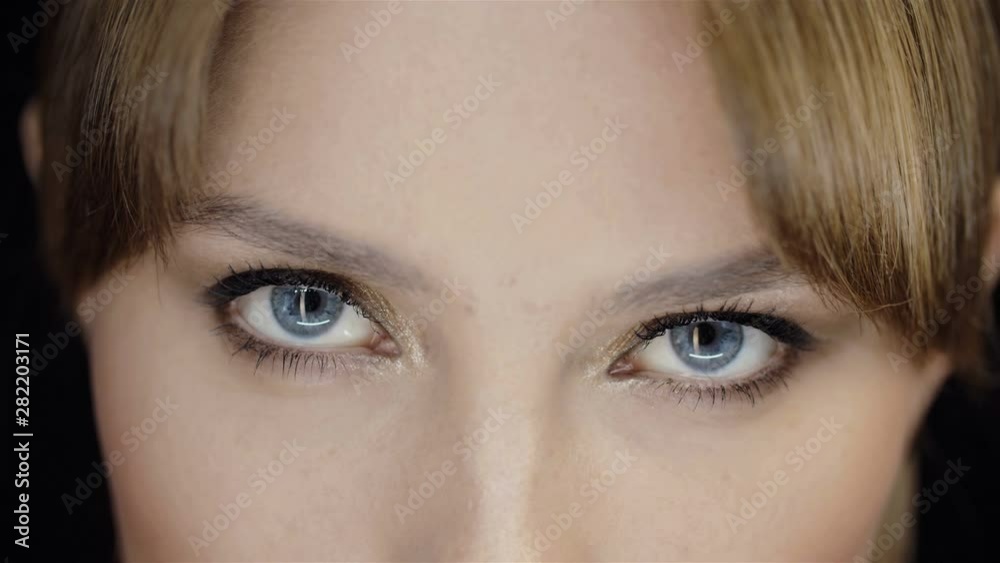 Close-up of girl's face with beautiful makeup. Thin eyebrows, long eyelashes, blue eyes. Gaze. Golden shadows. Clean skin of the girl's face. In the studio on black background.