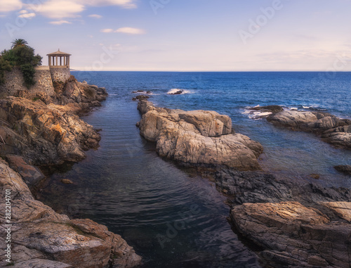 A mediterranean rocky coast beautifully embracing the calm waters of the sea with a little observatory at the left side in Catalonia, spain