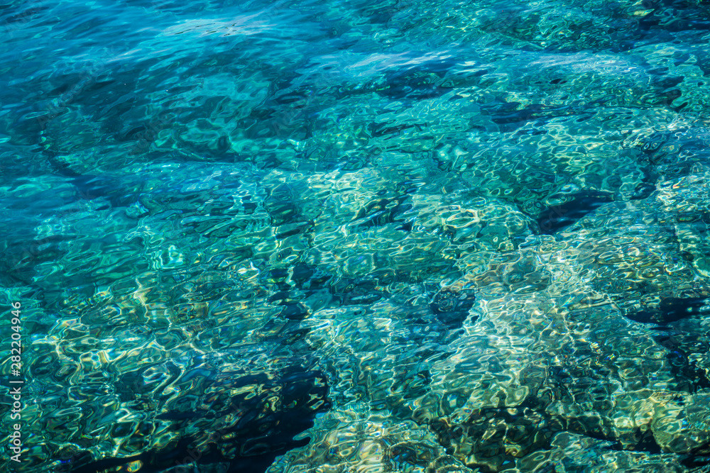 Turquoise sea surface with transparent shallow water - pebbles, stones, rocks on the seabed