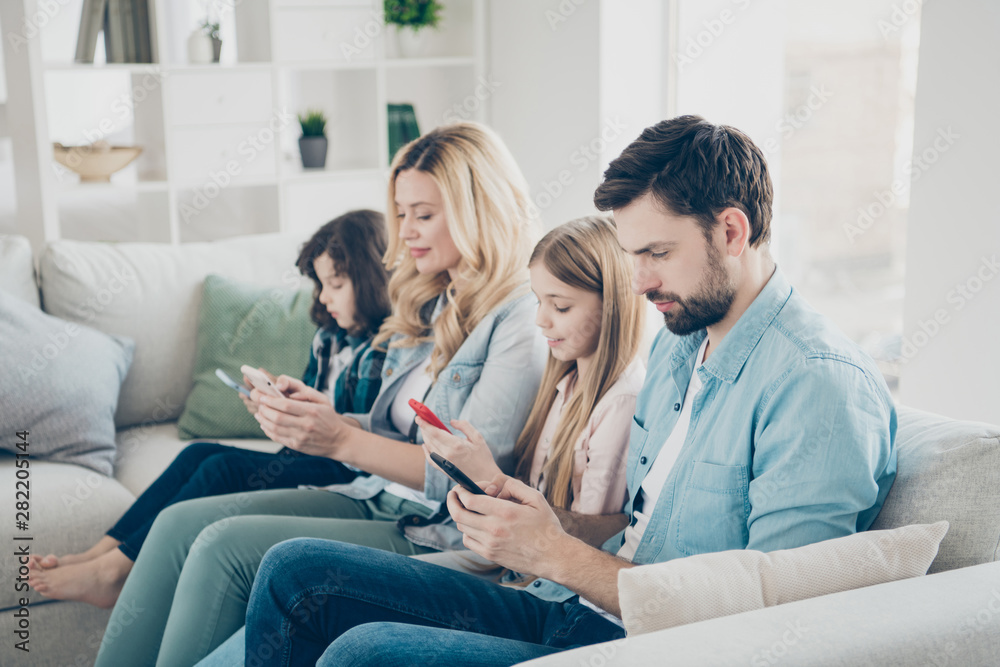 Fototapeta premium Young family two adopted children cozy sitting sofa look telephones don't care each other addiction concept
