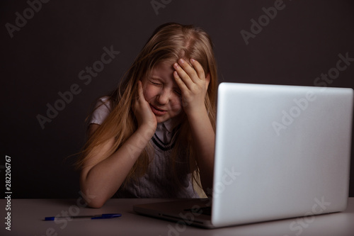 Girl with headache sitting at the desk and doing homework isolated. Tired child using computer