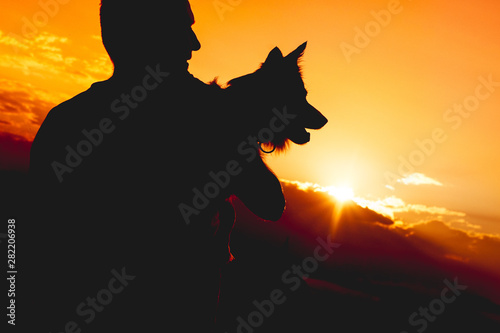 Unrecognizable person holding a dog. Silhouette against sundown.