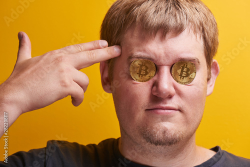 Horizontal portrait of fat guy with bitcoins in his eyes on a yellow background. Digital virtual currency concept, defrauded investor, cryptocurrency fall on Internet market photo