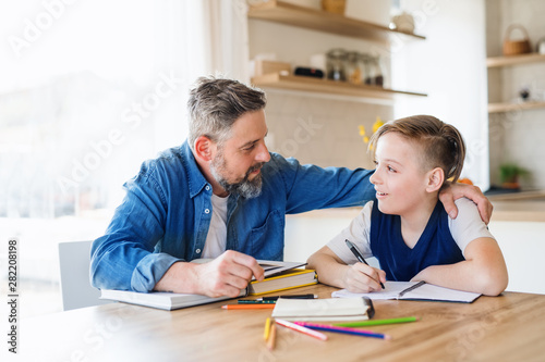Mature father with small son sitting at table indoors, making homework.