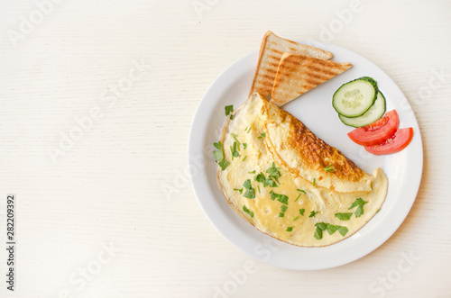 Omelet with cheese and parsley, sliced tomatoes and cucumbers on the plate. Scrambled eggs with copy space, top view. Healthy breakfast and lunch