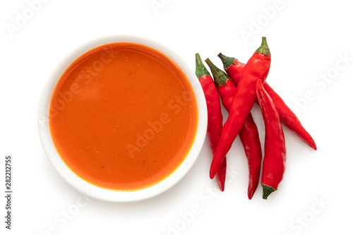 Peri peri chilli sauce in a white ceramic bowl next to a pile of red chillies isolated on white from above.