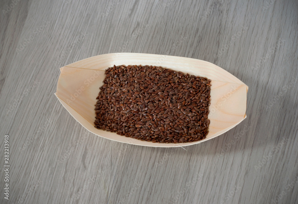 Flax seeds in a eco, wooden container isolated on wooden background Flax seeds in a eco, wooden container isolated on wooden background