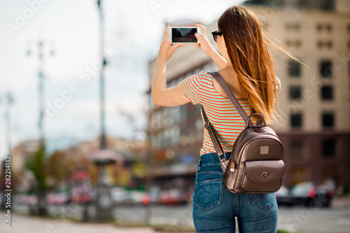 Back side photo of interested person making photo blogging wearing striped t-shirt denim jeans in city outdoors photo