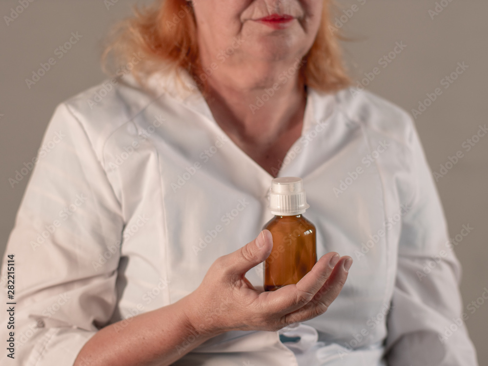 Cheerful elderly woman in white coat with beautiful wrinkled face holds pills in her hands to choose medicine. Vial with medicine and glass of water. Selective Focus Depth of Field Cheerful elderly woman in white coat with beautiful wrinkled face holds pills in her hands to choose medicine. Vial with medicine and glass of water. Selective Focus Depth of Field