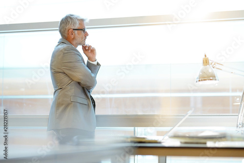 Foto Mature businessman looking out large window in office