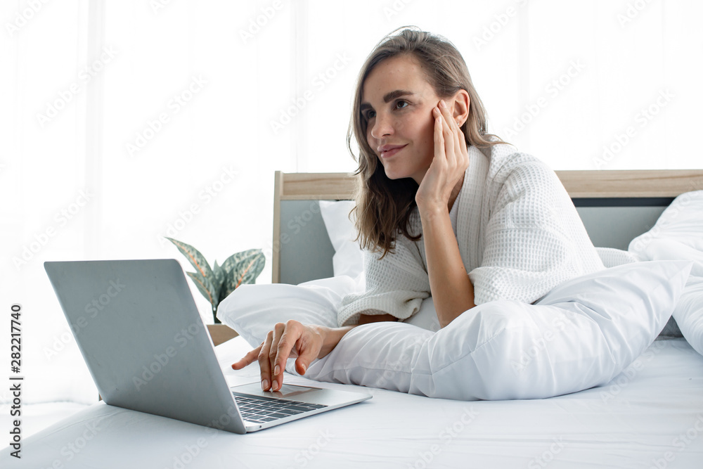 Caucasian woman in pajama playing social in laptop on white bed. Caucasian woman in pajama playing social in laptop on white bed.