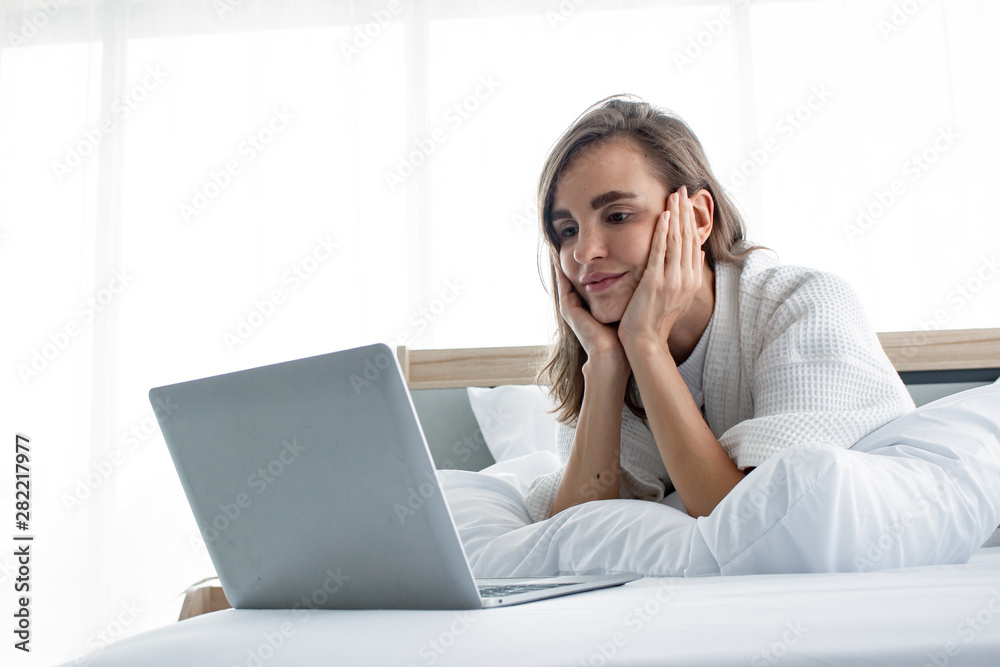 Caucasian woman in pajama playing social in laptop on white bed. Caucasian woman in pajama playing social in laptop on white bed.